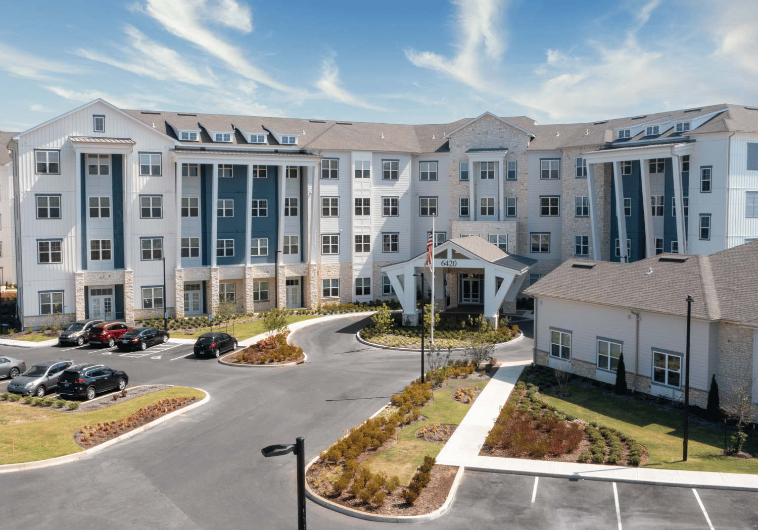 Aerial view of a modern multi-story apartment complex with a curved driveway and landscaped grounds.